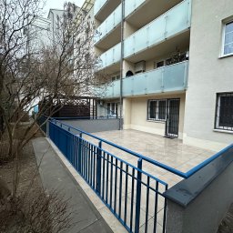 Mykhailo Mykhailiyk - Wyremontowany balkon z niebieską barierką i jasnymi płytkami. Widok z dołu na budynek z balkonami. Drzewa bez liści po lewej stronie kadru. Dobre oświetlenie.
