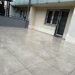 Mykhailo Mykhailiyk - Jasne, błyszczące płytki na balkonie z przeszkloną balustradą i oknem z kratą. Ułożenie płytek w karo, widok z dołu, lekki kąt.