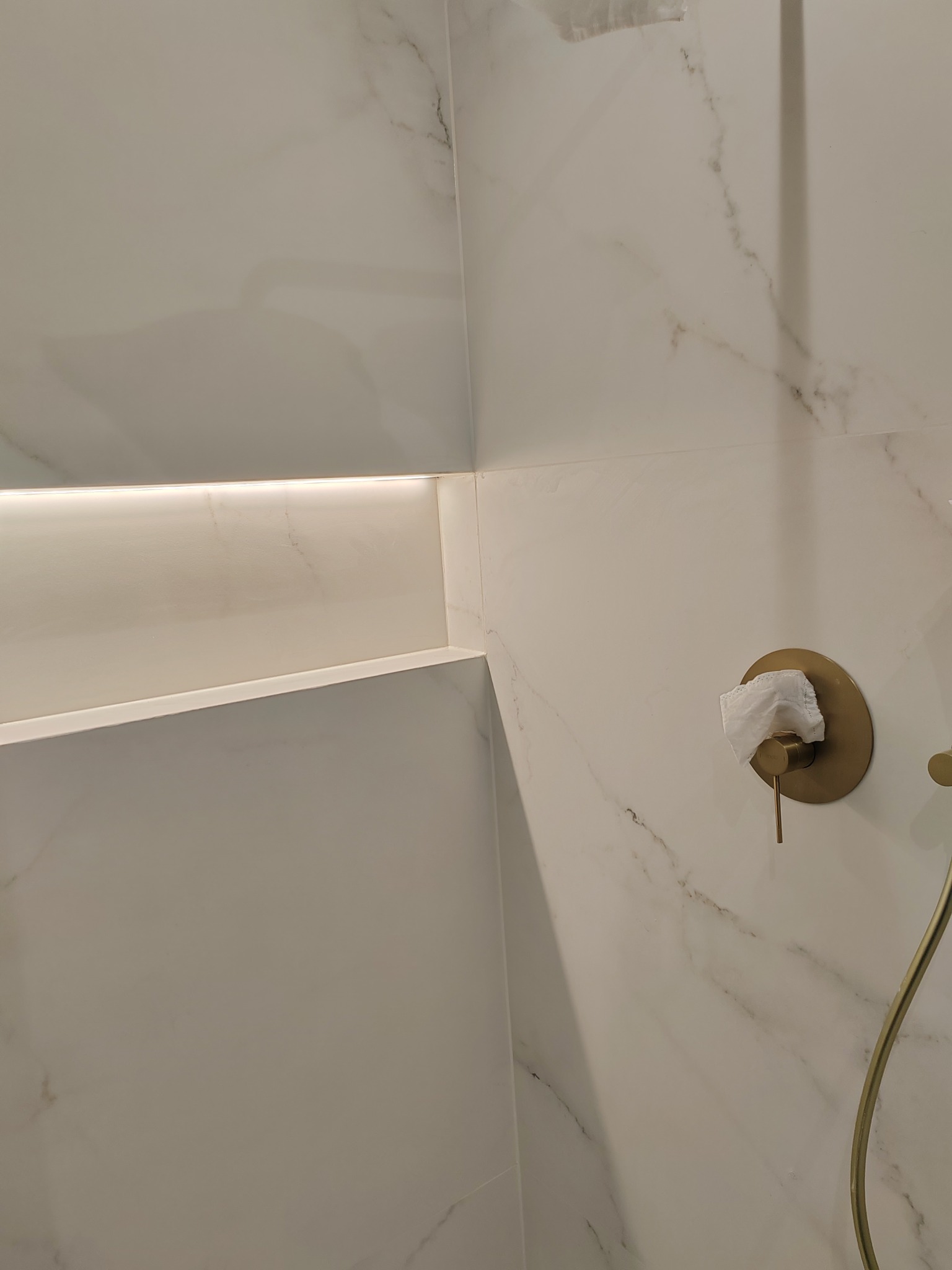 Wykończona wnęka z oświetleniem LED i bateria prysznicowa w kolorze złota na marmurowej ścianie w łazience we Wrocławiu. Minimalistyczny design.