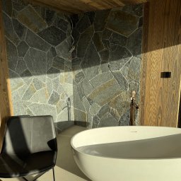 USŁUGI KAMIENIARSKO-FLIZIARSKIE Józef Sukiennik - Nowoczesna łazienka z kamienną ścianą, wolnostojącą wanną i drewnianym wykończeniem. Słoneczne światło podkreśla fakturę kamienia i elegancję wnętrza.