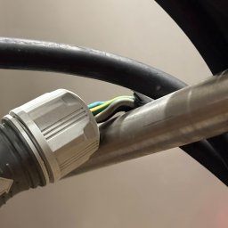 TWM Serwis Tomasz Musiał - Szczegółowe zbliżenie na przewody elektryczne w peszlu, z widocznym złączem i kolorowymi izolacjami, umieszczone w szarej rurce instalacyjnej.