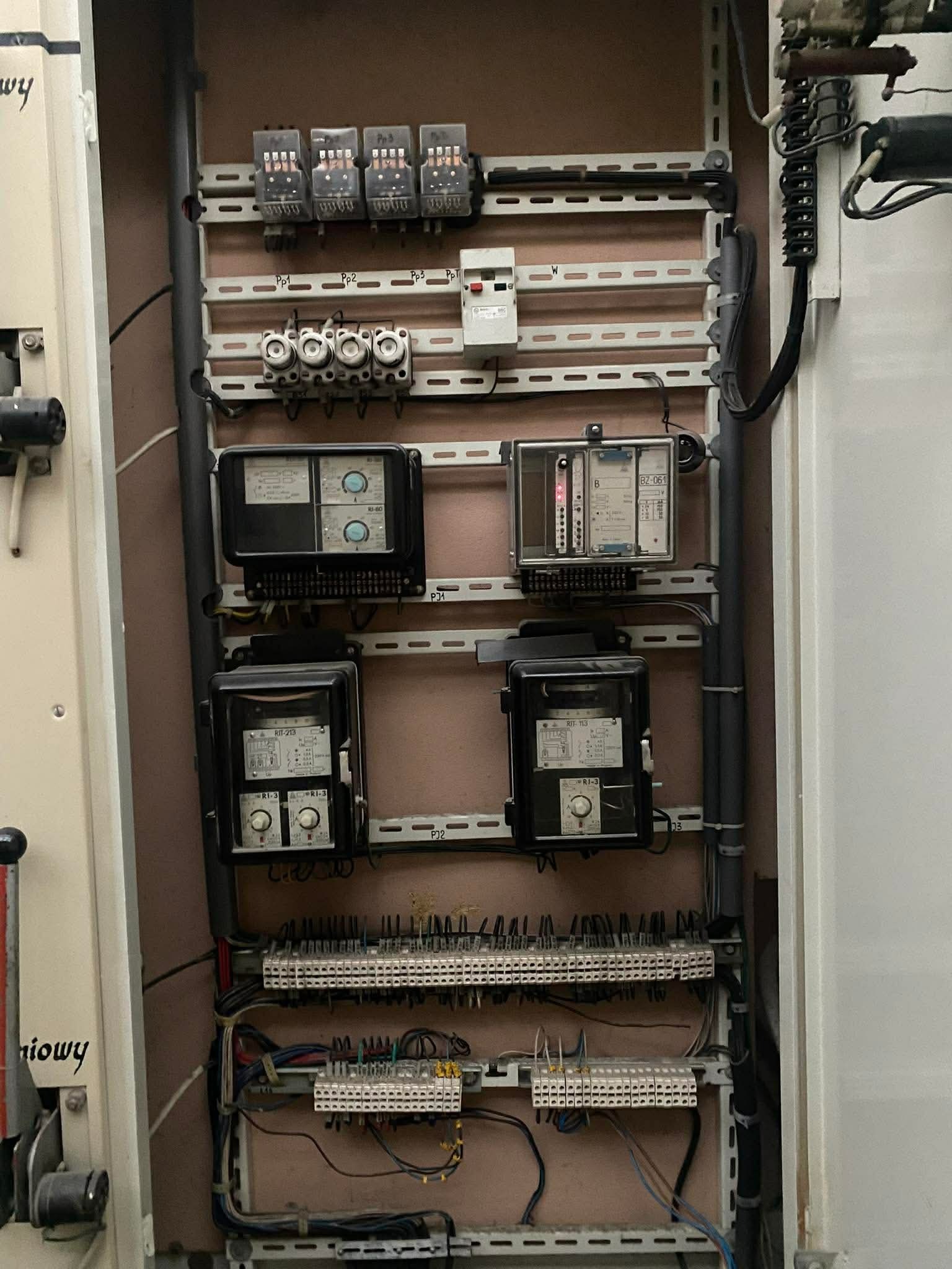Rozdzielnia elektryczna z zabezpieczeniami, bezpiecznikami i przewodami. Widoczne liczniki, przekaźniki i listwy zaciskowe. Instalacja wewnątrz szafy sterowniczej.