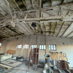 Ekspres Multiserwis - Wnętrze opuszczonego magazynu z graffiti na ścianach, drewnianą konstrukcją dachu i porozrzucanymi elementami wyposażenia. Widok z dołu, surowy klimat.