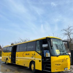 Przewozy „Yellon Bus”' Sławomir Jelonek - Żółty autobus z otwartymi drzwiami na tle błękitnego nieba. Na szybie widoczna naklejka z sylwetkami dzieci. Autobus oznaczony logo 'BUS' z motywem półksiężyca.