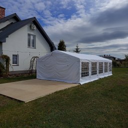 JM EVENT - Biały namiot imprezowy z oknami, ustawiony na betonowej płycie obok domu z szarą dachówką. Niebo z chmurami w tle.