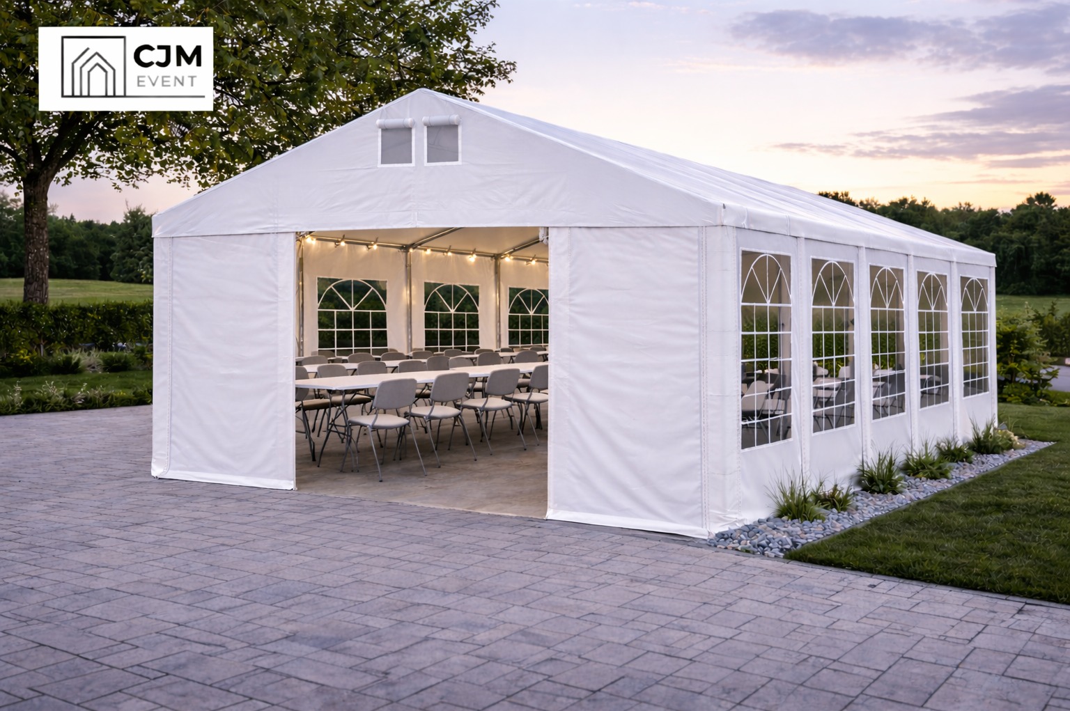 Biały namiot eventowy z oknami i oświetleniem, ustawiony na zewnątrz, z widocznymi stołami i krzesłami w środku, przygotowany na imprezę. Widok z zewnątrz, w tle zieleń.