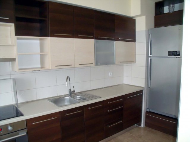 Nowoczesna kuchnia na wymiar z dwukolorowymi szafkami (ciemny brąz i beż), srebrnym zlewem, białymi płytkami i lodówką ze stali nierdzewnej.