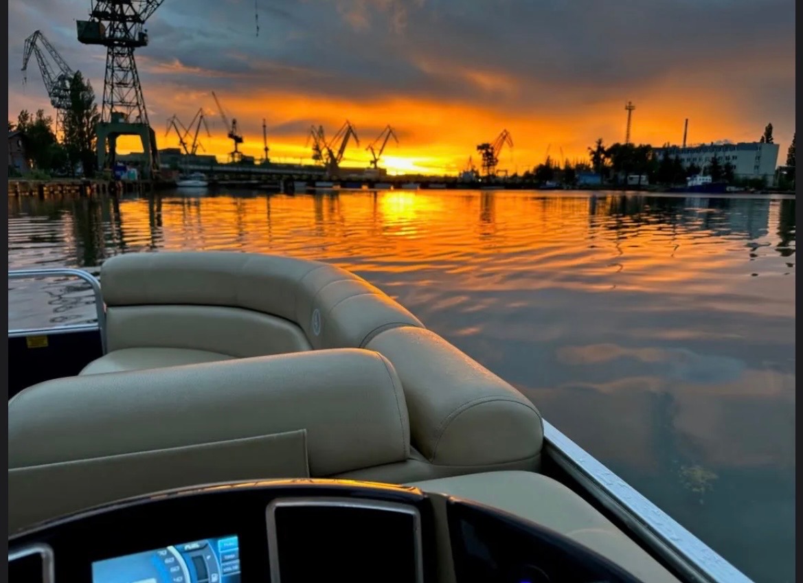 Ponton na wodzie o zmierzchu, z widokiem na dźwigi portowe i budynki w tle. Ciepłe światło zachodzącego słońca odbija się w spokojnej wodzie.