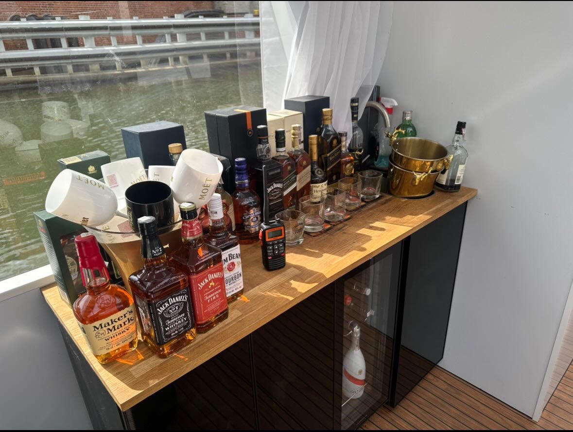 Mobilny bar z selekcją alkoholi premium, w tym Jack Daniel's i Moët, ustawiony na łodzi z widokiem na kanał. Złoty kubełek na lód i eleganckie szkło dodają luksusowego charakteru.