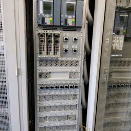 EL-KAR Karol Napora - Rozdzielnica elektryczna z licznymi zabezpieczeniami, wyłącznikami i modułami sterującymi. Widoczne przewody w peszlach. Element instalacji w szafie sterowniczej.