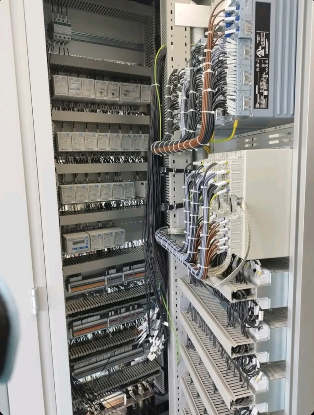 Rozdzielnica elektryczna z licznymi przewodami i elementami sterującymi, widok z bliska na uporządkowane okablowanie wewnątrz szafy sterowniczej.