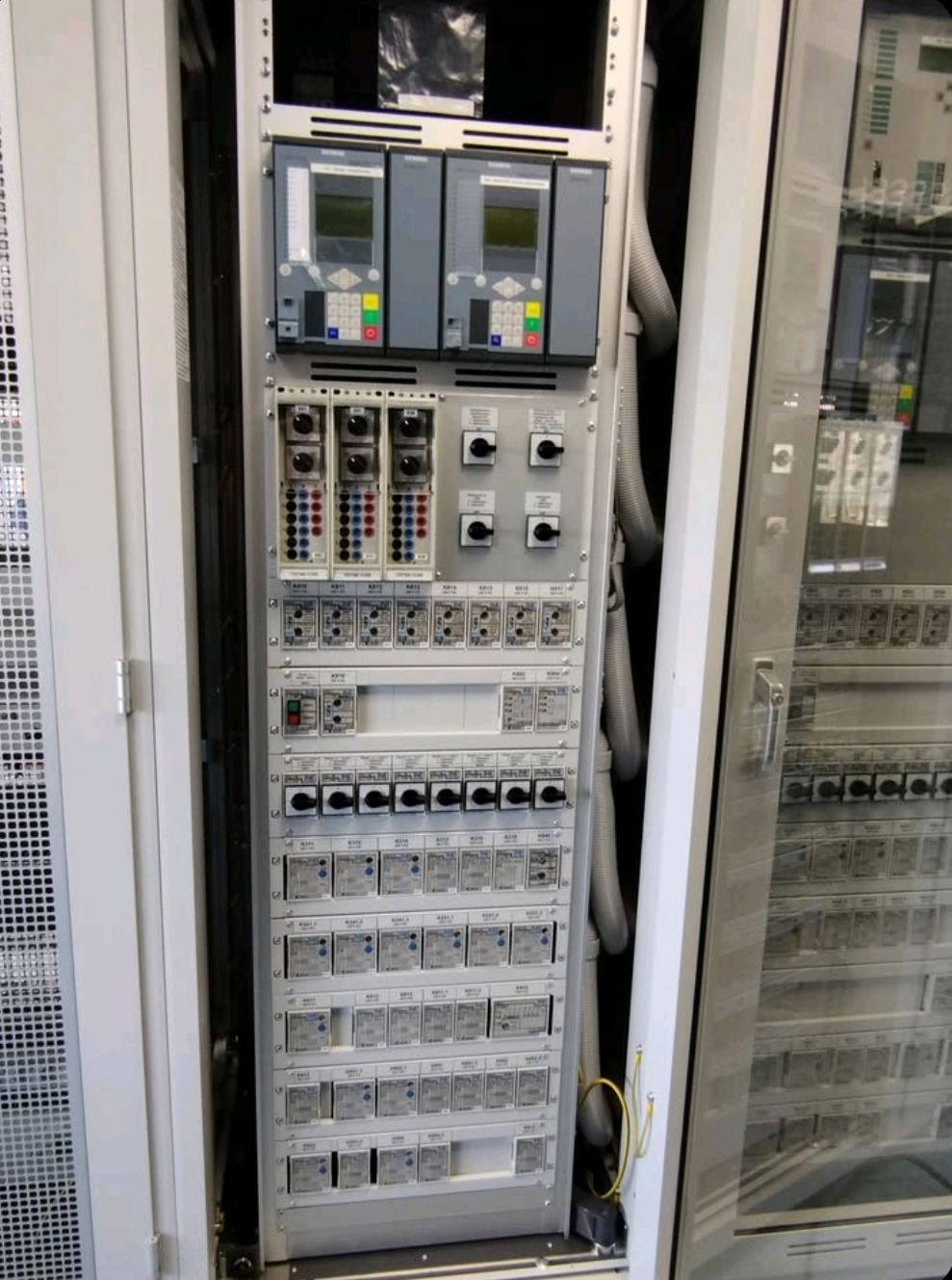 Rozdzielnica elektryczna z licznymi zabezpieczeniami, wyłącznikami i modułami sterującymi. Widoczne przewody w peszlach. Element instalacji w szafie sterowniczej.