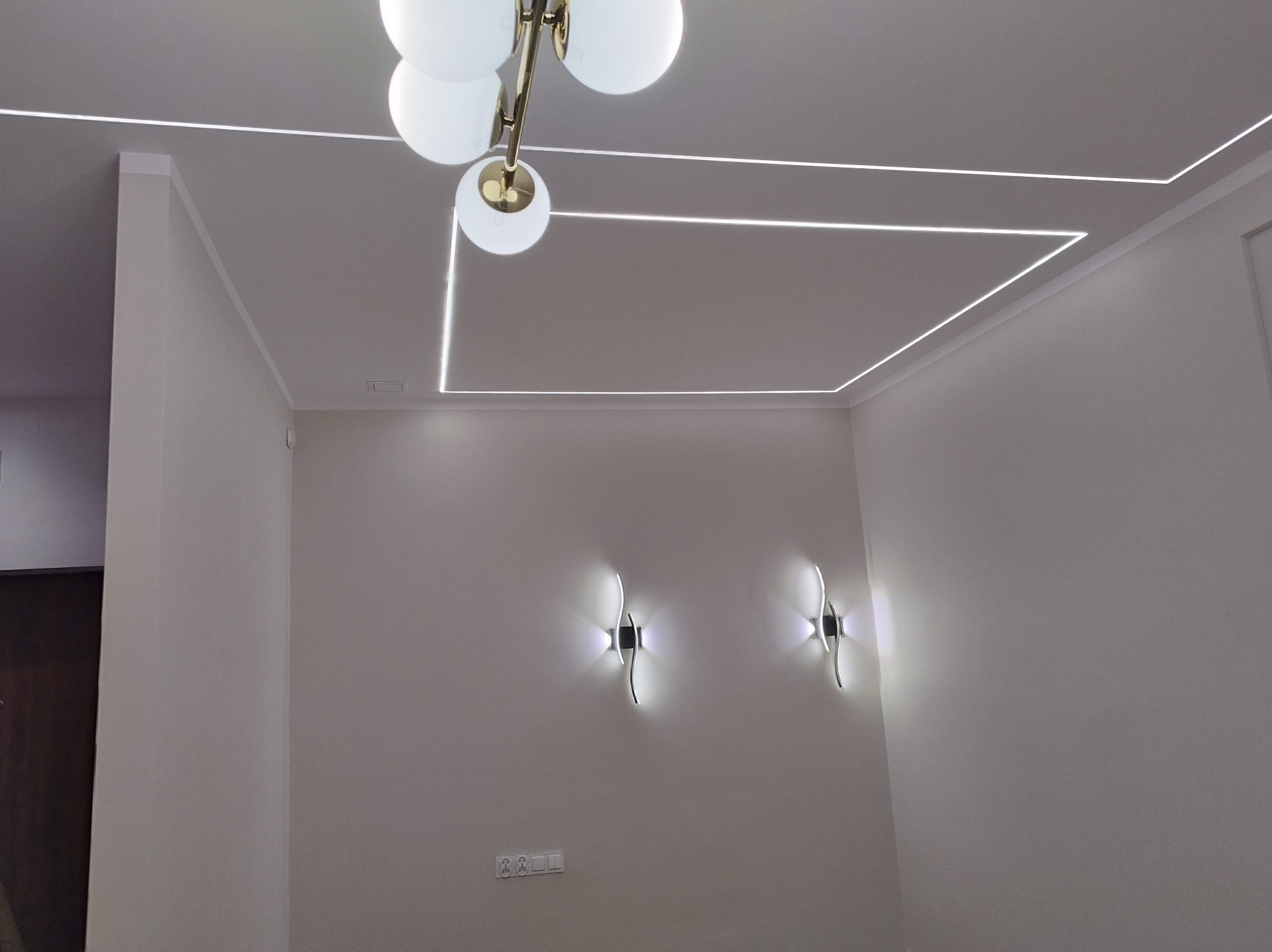 Nowoczesne oświetlenie sufitowe z lampą kulistą i liniami LED tworzącymi geometryczny wzór. Dwa kinkiety ścienne o futurystycznym designie. Minimalistyczne wnętrze.