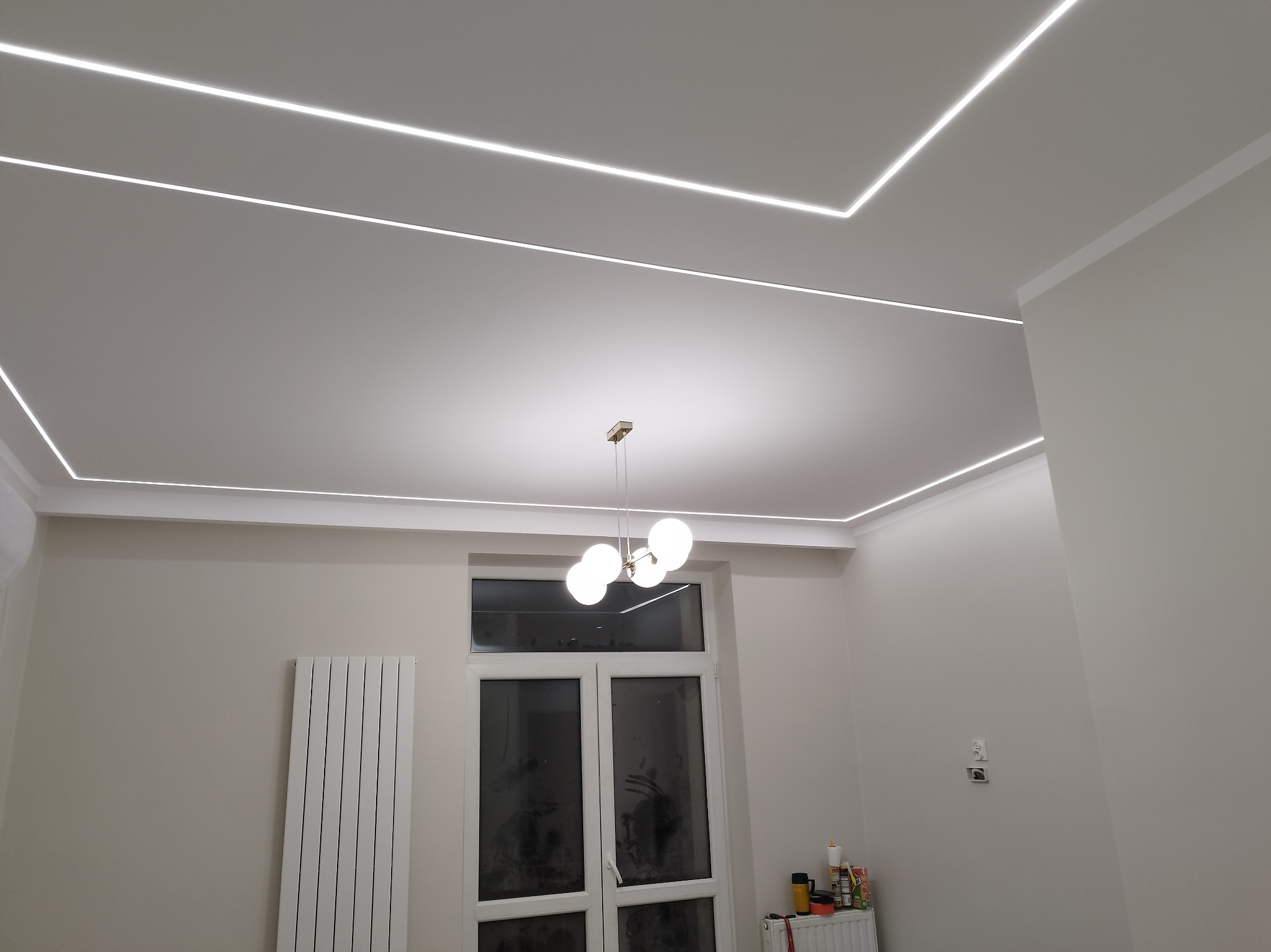Nowoczesne oświetlenie sufitowe LED w kształcie prostokątów, uzupełnione wiszącą lampą kulistą. Minimalistyczny design w jasnym wnętrzu.