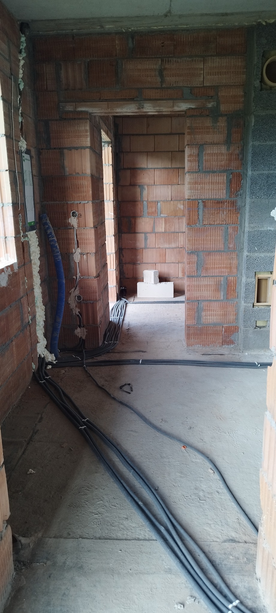 Surowy stan budynku w trakcie prac. Widoczne kable w peszlach ułożone na podłodze, puszki elektryczne w ścianach z cegły. Instalacja w trakcie realizacji.