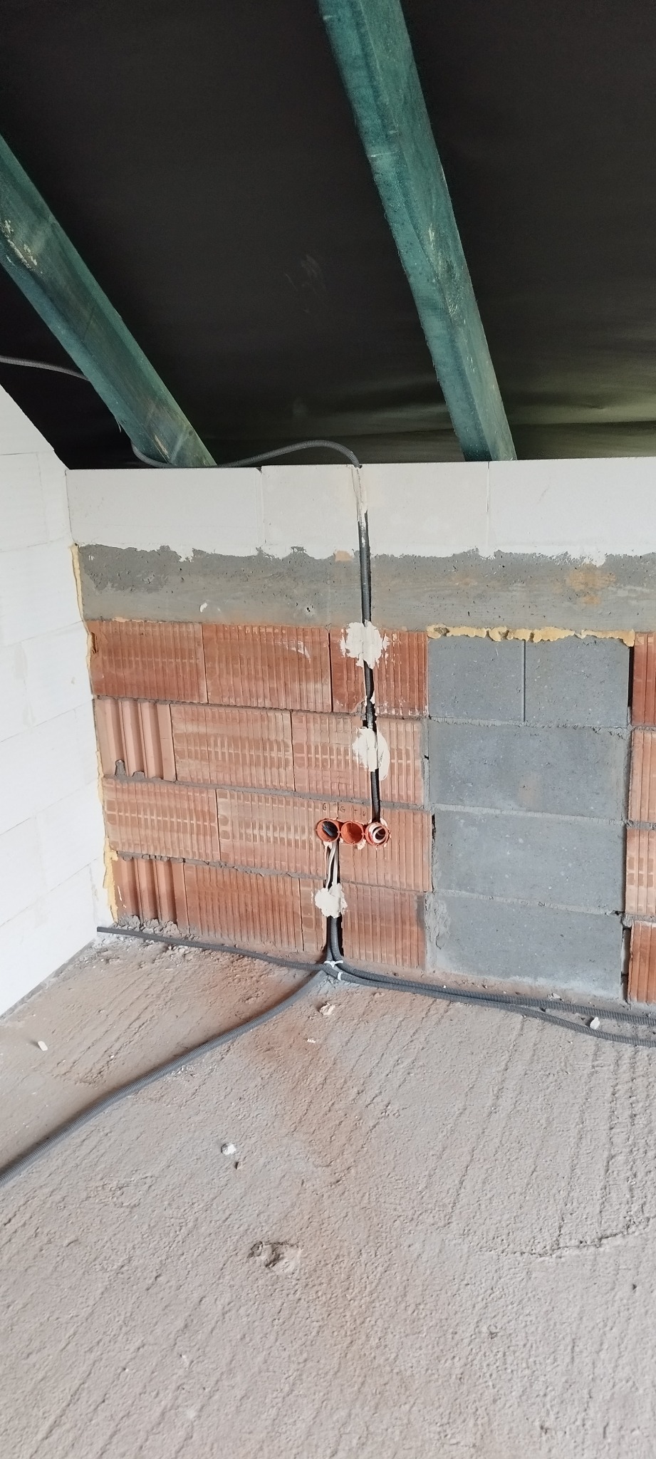 Wnętrze w trakcie prac: kable w peszlach prowadzone w ścianie z cegieł i bloczków, widoczne puszki instalacyjne. Sufit z drewnianymi belkami.