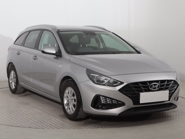 Srebrny Hyundai i30 kombi, widok z przodu i boku, na jasnym tle. Auto z relingami dachowymi i charakterystycznym grillem.