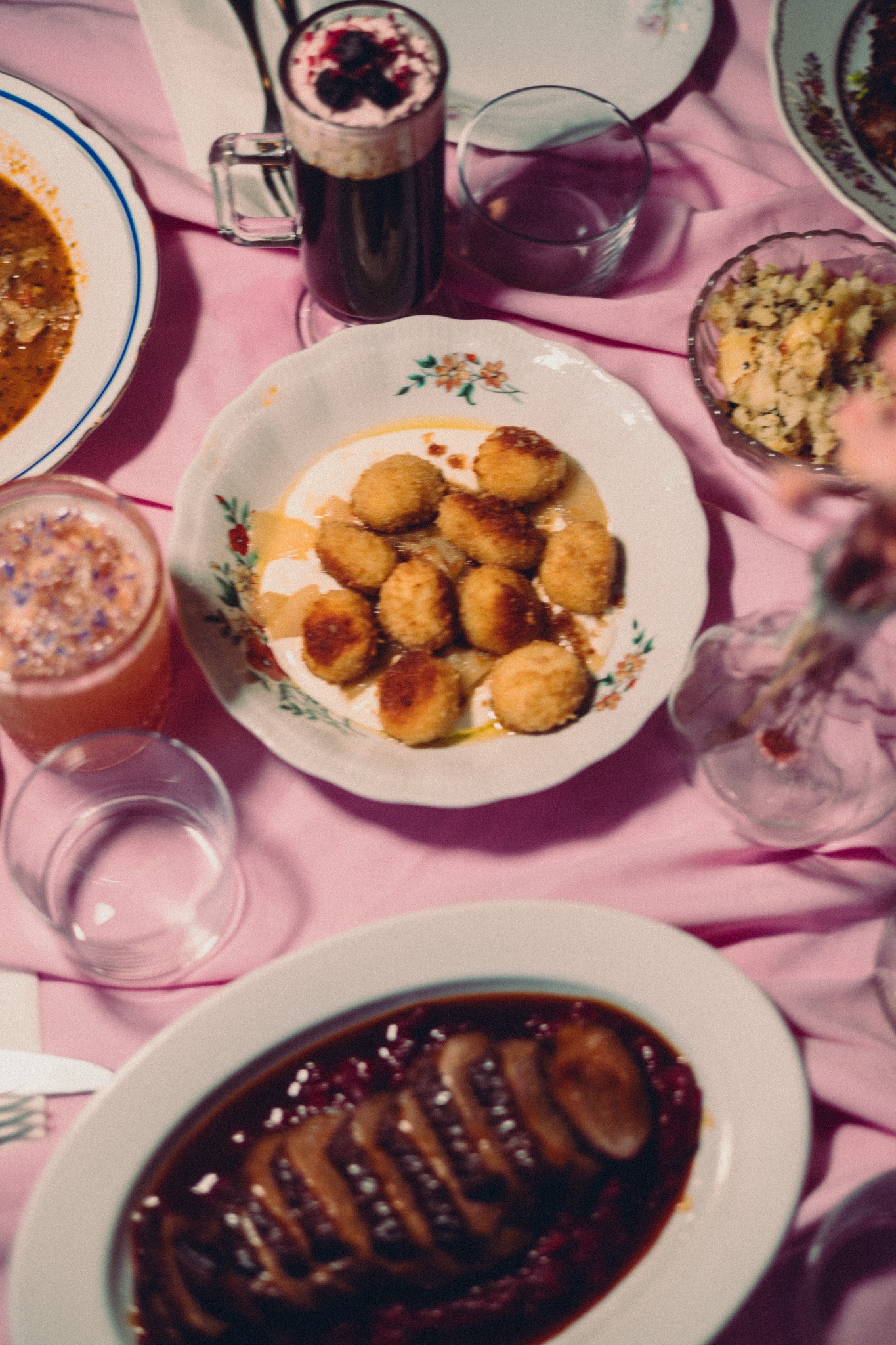Elegancko zastawiony stół z różowym obrusem, na którym znajdują się różnorodne dania, napoje i dekoracje kwiatowe. Ujęcie z góry, podkreślające bogactwo i estetykę prezentacji.