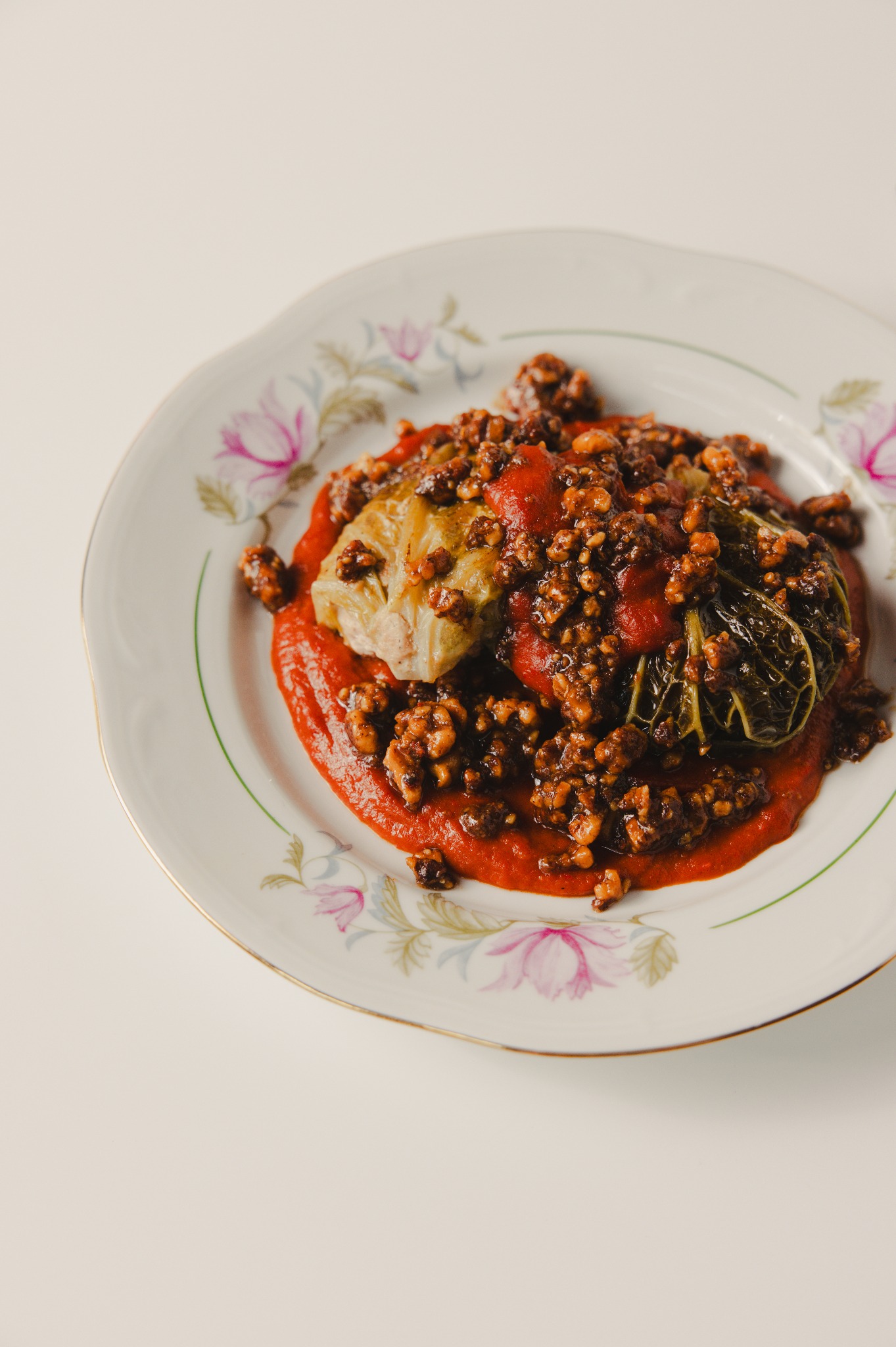 Dwa gołąbki w sosie pomidorowym, posypane mięsem, na talerzu w kwiaty. Ujęcie z góry, jasne tło. Danie gotowe do spożycia, prezentacja potrawy.