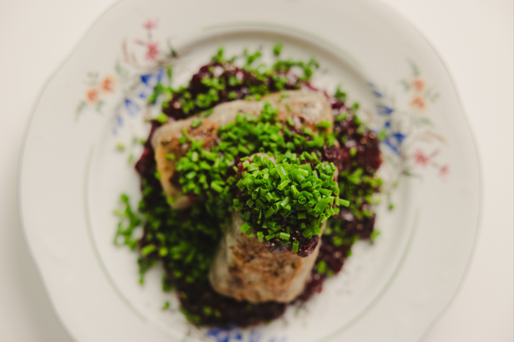 Dwa roladki mięsne na buraczkach, posypane świeżym szczypiorkiem, podane na talerzu z kwiatowym wzorem. Elegancka kompozycja dania.