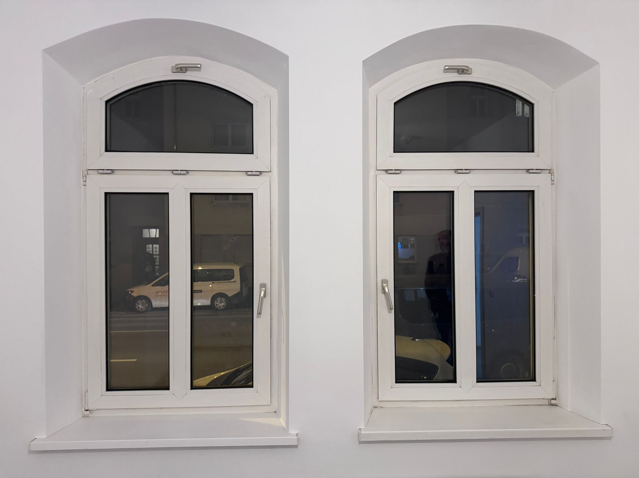 Dwa białe okna łukowe z widokiem na ulicę, odbijające światła miasta. Minimalistyczny design, symetryczny układ, czyste linie i białe ramy okienne.