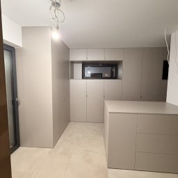 Formedge - Minimalistyczna zabudowa meblowa w odcieniach szarości, zintegrowana ze ścianą, z małym oknem w górnej części. Widoczne szafki i szuflady, nowoczesne oświetlenie.