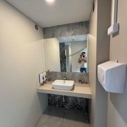 Formedge - Nowoczesna łazienka z umywalką nablatową i lustrem, wykończona w neutralnych barwach z akcentem roślinnym. Widoczne fugi na podłodze wskazują na świeżo zakończony montaż płytek.