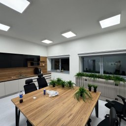 Formedge - Nowoczesna kuchnia z drewnianym blatem w Kalwarii Zebrzydowskiej. Czarne szafki wiszące, jasne dolne. Stół konferencyjny z roślinami. Minimalistyczny design.