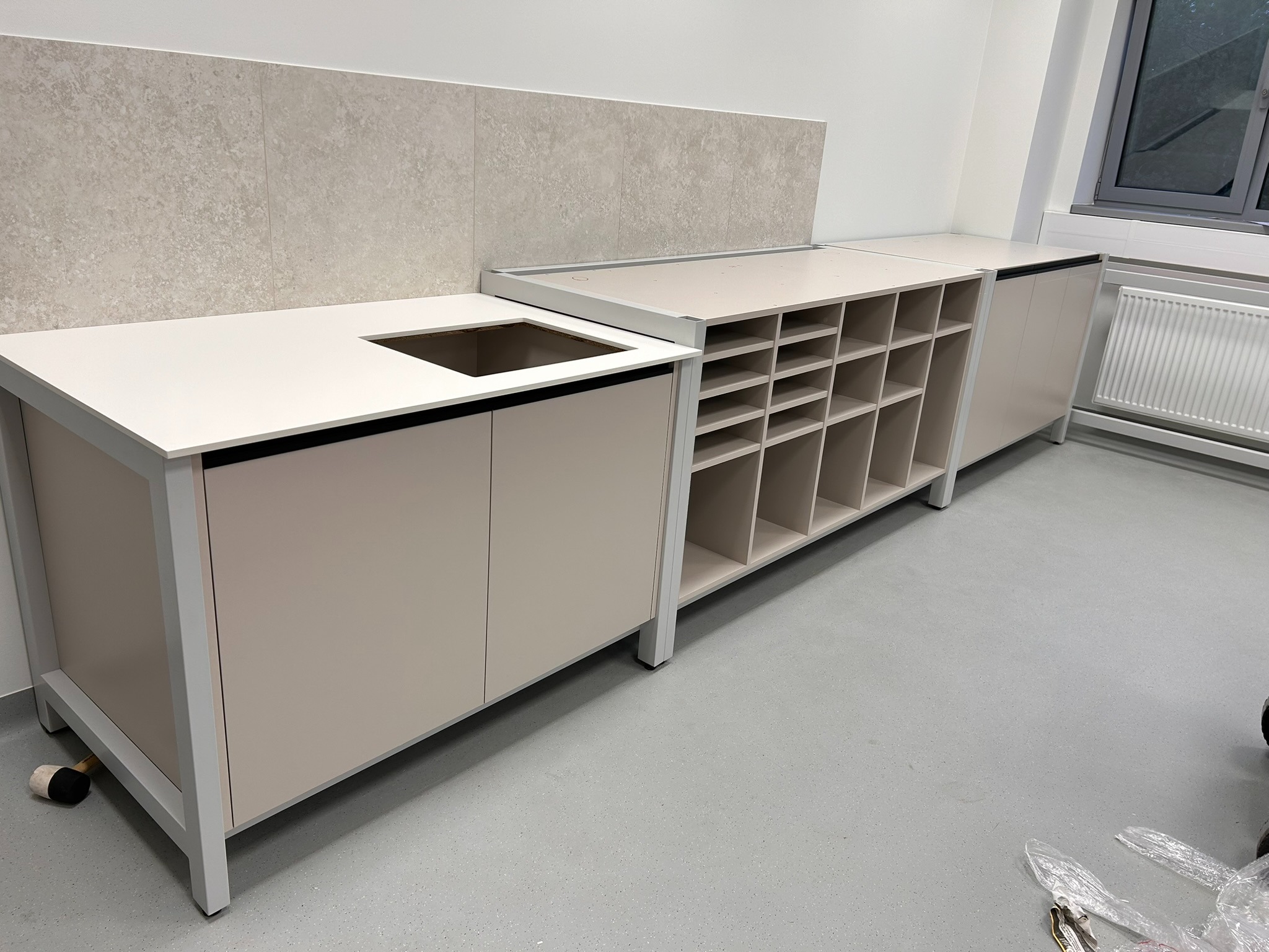 Jasna zabudowa kuchenna z blatem i szafkami w minimalistycznym stylu, z widocznym miejscem na zlew i półkami na wino. Ujęcie z niskiego kąta, podkreślające nowoczesny design.