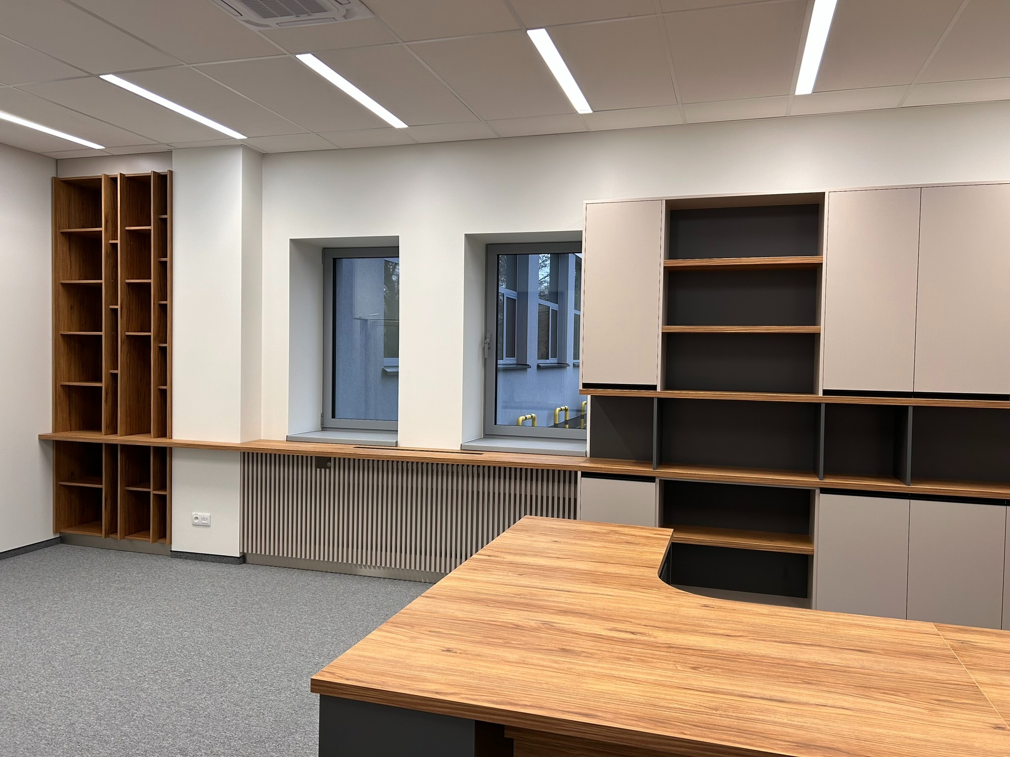 Nowoczesne meble biurowe na wymiar w Kalwarii Zebrzydowskiej: regał z drewna, szafki w odcieniach szarości i biurko z blatem drewnopodobnym. Minimalistyczny design.