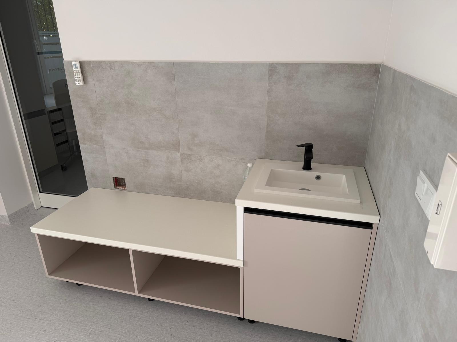 Nowoczesna łazienka z szafką pod umywalkę w odcieniach beżu i bieli, czarna bateria, szare płytki na ścianie. Minimalistyczny design, widoczne detale wykończenia.