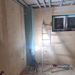 Jakub Krzywański - Wnętrze w trakcie montażu sufitu podwieszanego z metalowej konstrukcji. Widoczna drabina, lampa na statywie i fragment ściany z płytą karton-gips.