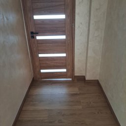 Jakub Krzywański - Nowoczesne wnętrze: drewniana podłoga, drzwi z przeszkleniami i ściany w odcieniach beżu z delikatną fakturą. Minimalistyczny design, ciepłe kolory, wykończone detale.