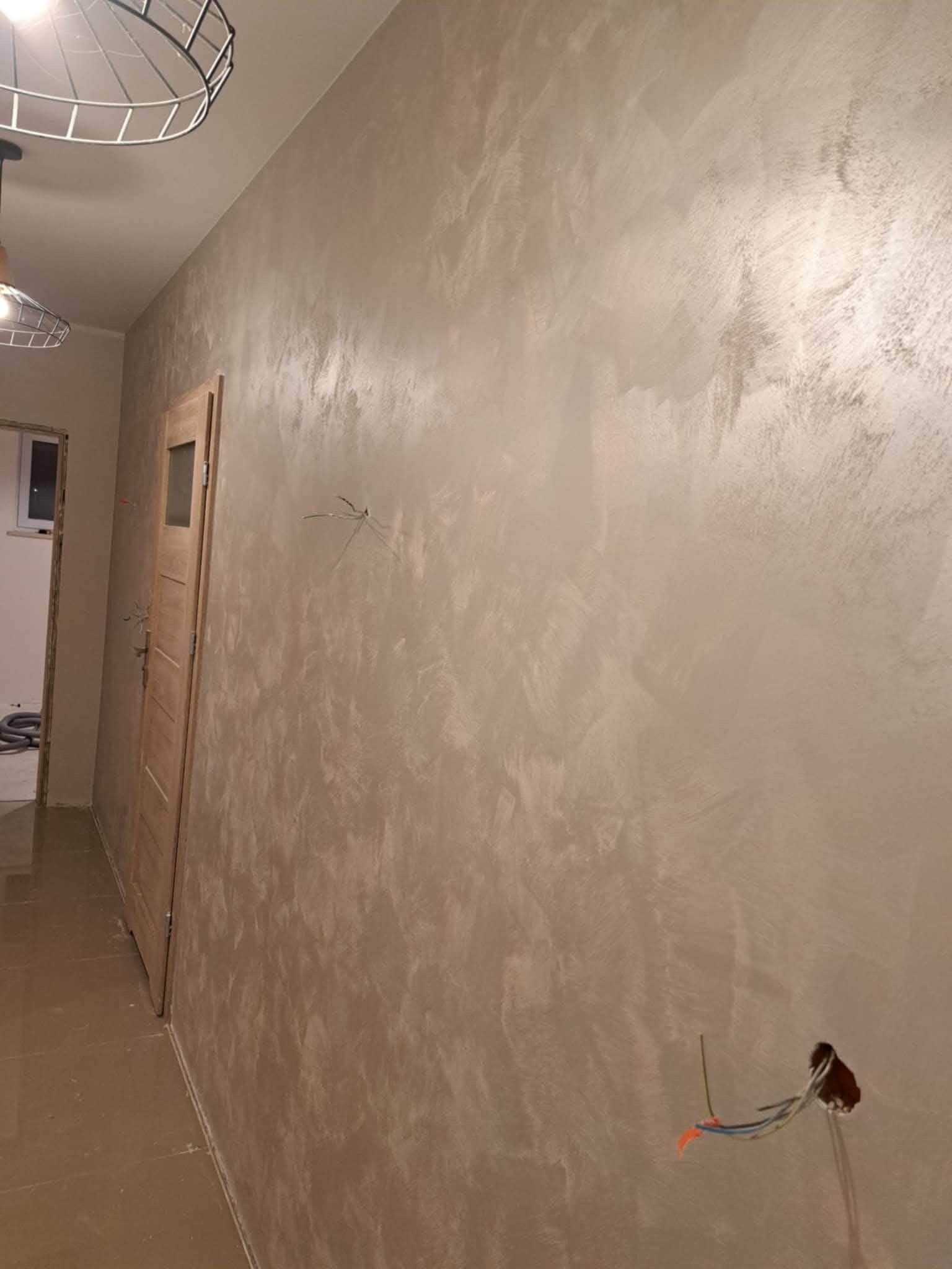 Ściana po dekoracyjnym malowaniu w odcieniach beżu i srebra, widoczne kable elektryczne wystające ze ściany, drzwi z ościeżnicą. Wykończenie wnętrza.