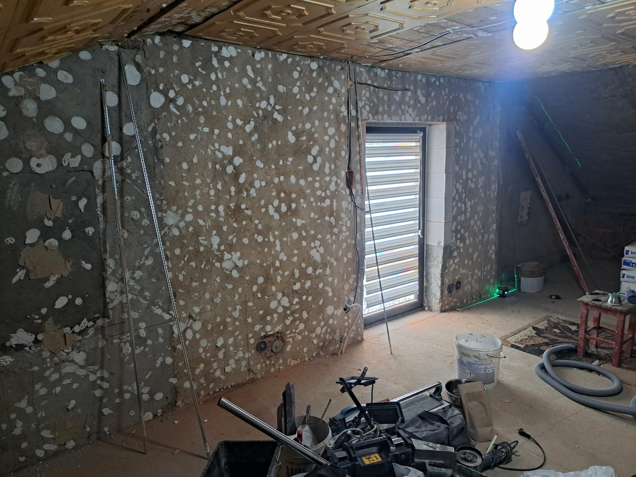 Poddasze w trakcie prac wykończeniowych: ściany z widocznymi punktami szpachlowania, profile metalowe, narzędzia glazurnicze, poziomica laserowa, sufit z kasetonami.