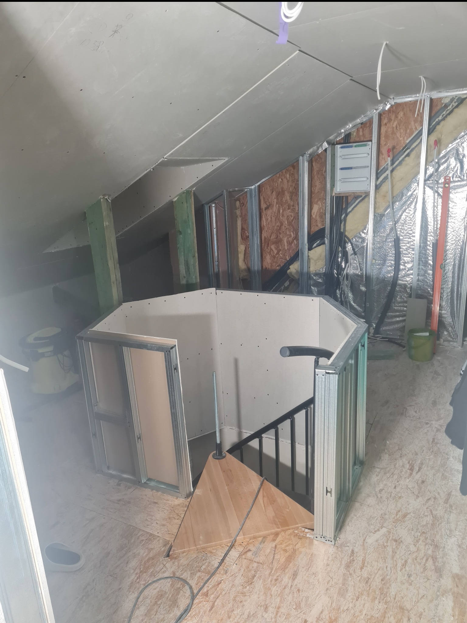 Adaptacja poddasza: zabudowa schodów płytą gipsowo-kartonową na metalowym stelażu. Widoczne elementy konstrukcyjne i izolacja. Prace w toku, sufit z płyt.