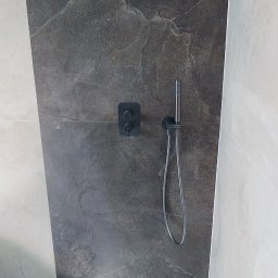 Gres Pro - Nowoczesna kabina prysznicowa z deszczownicą i szarą płytką imitującą kamień. Minimalistyczny design, czarna armatura, jasne płytki na ścianach i podłodze.