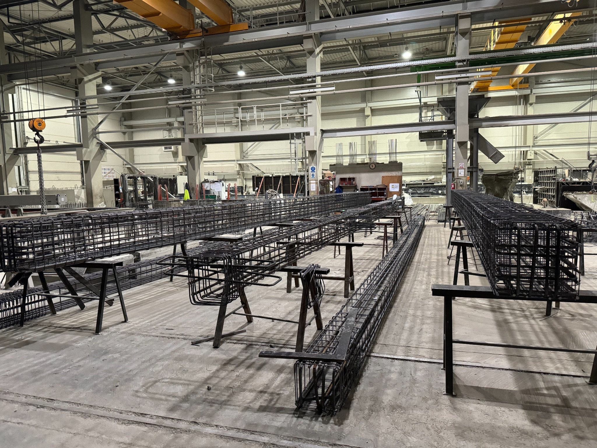 Przygotowane zbrojenie na metalowych kozłach w hali produkcyjnej. Widoczne elementy konstrukcyjne budynku i suwnica. Zbrojenie do budowy budynków żelbetowych.