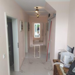 Vasyl Lutchyn - Jasny korytarz po remoncie z marmurową podłogą i różowymi ścianami. Widoczne drzwi, oświetlenie sufitowe i poziomica oparta o ścianę. W tle osoba robiąca zdjęcie.