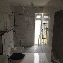 Vasyl Lutchyn - Wykończona łazienka z marmurowymi płytkami, wiszącą toaletą i bidetem, czarną armaturą i grzejnikiem drabinkowym. Nowoczesne oświetlenie sufitowe.