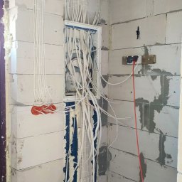 PSK Sp. z o.o. - Rozprowadzenie przewodów elektrycznych w ścianie z betonu komórkowego, widoczna skrzynka rozdzielcza i peszle. Instalacja w trakcie montażu, surowy stan.