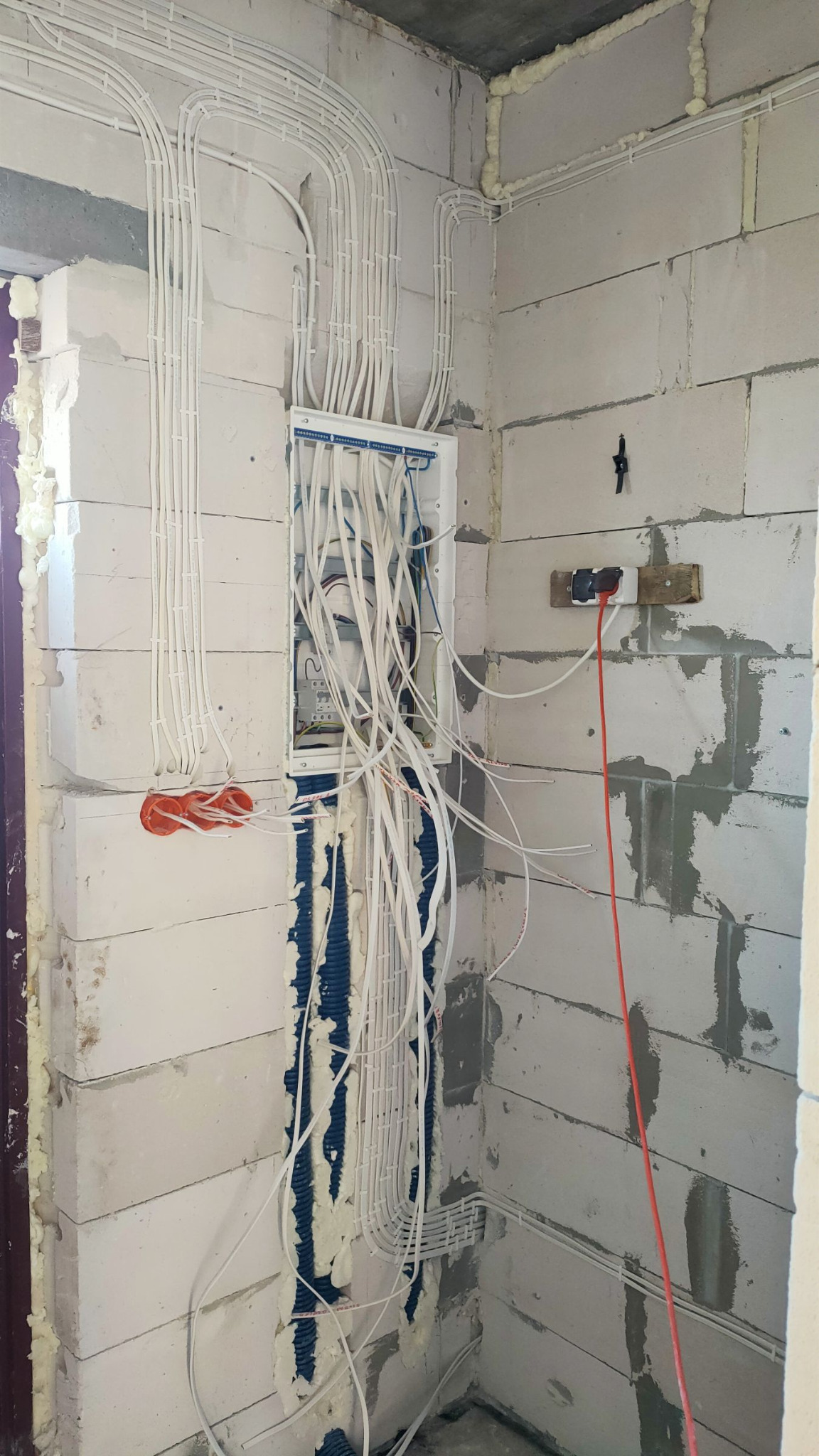 Rozprowadzenie przewodów elektrycznych w ścianie z betonu komórkowego, widoczna skrzynka rozdzielcza i peszle. Instalacja w trakcie montażu, surowy stan.