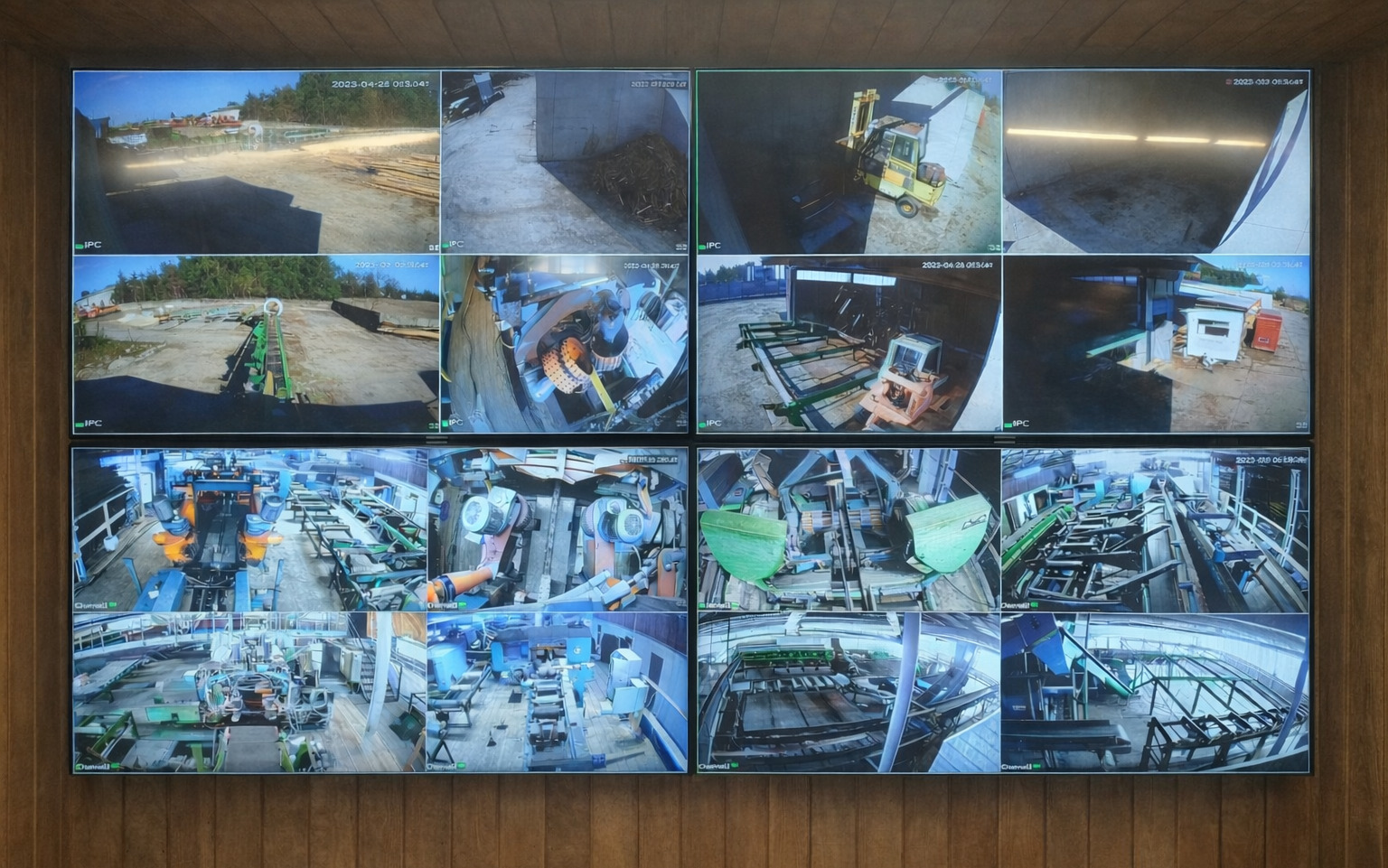 Ekran monitoringu z wieloma kamerami przemysłowymi, ukazujący różne obszary zakładu produkcyjnego z datami i oznaczeniami kamer. Widok z kamery na ścianie o teksturze drewna.
