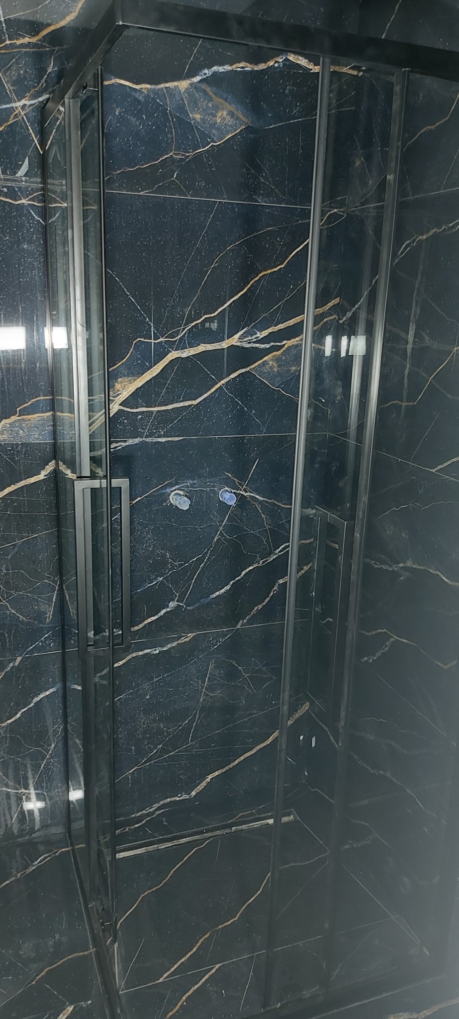 Kabina prysznicowa z czarnymi profilami i marmurowymi płytkami w odcieniach czerni i złota. Nowoczesny design łazienki po remoncie, widok z bliska.