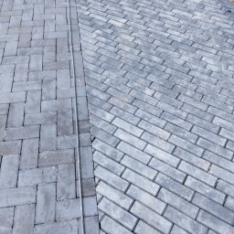 Matbud - Ułożona szara kostka brukowa w dwóch wzorach: prosto i pod kątem. Widoczna linia oddzielająca wzory. Całość kadrowana z góry, z bliska.