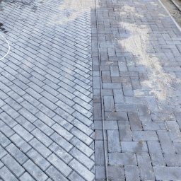 Matbud - Ułożona kostka brukowa w dwóch odcieniach szarości, oddzielona linią. Część powierzchni posypana piaskiem, co sugeruje etap prac wykończeniowych.
