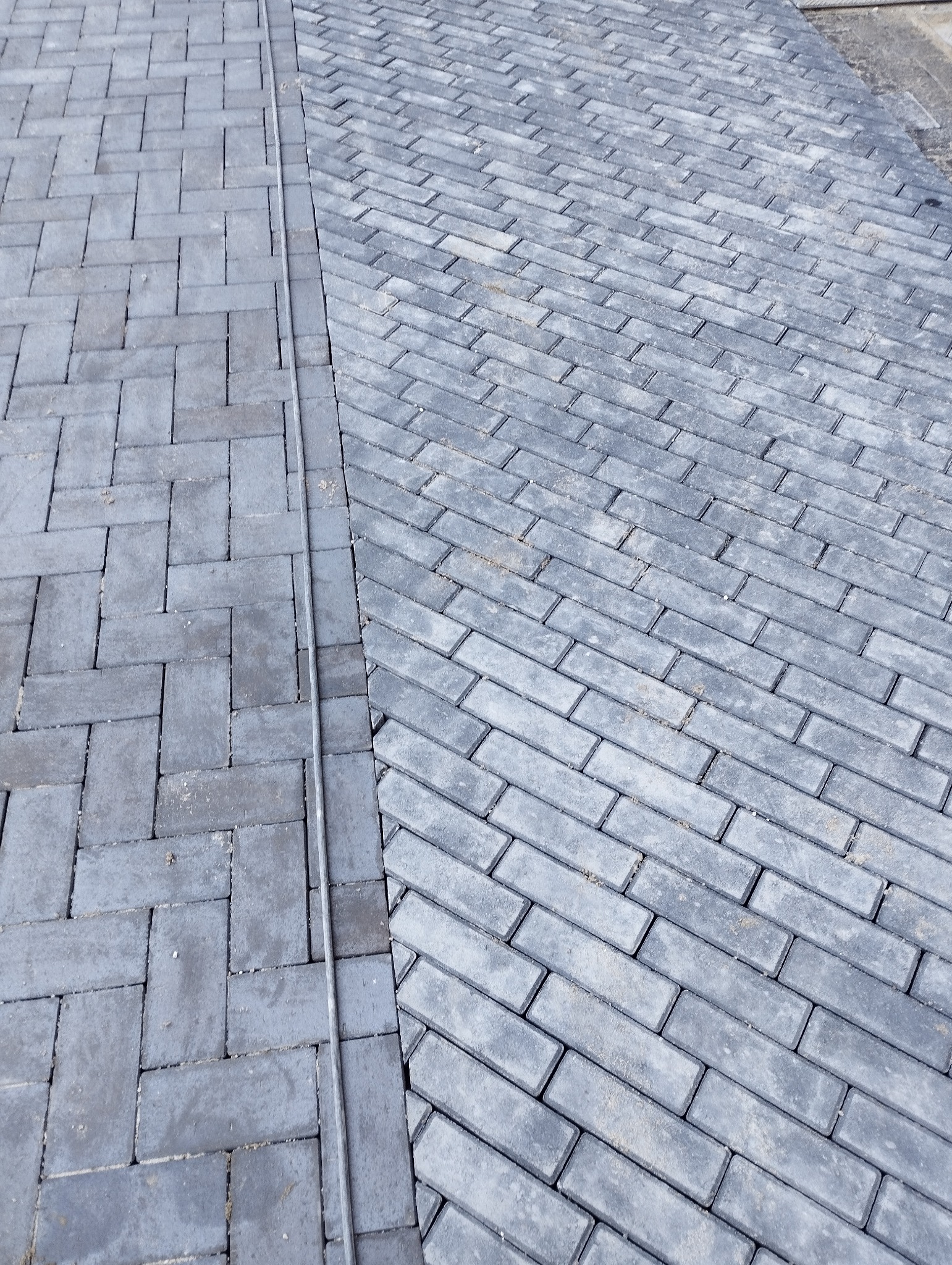 Ułożona szara kostka brukowa w dwóch wzorach: prosto i pod kątem. Widoczna linia oddzielająca wzory. Całość kadrowana z góry, z bliska.
