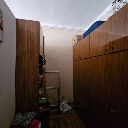 Gryfny porządek - Wnętrze zagraconego pokoju z drewnianymi szafami, suszarką na pranie i workiem na podłodze. Widok na ścianę z kalendarzem. Przygotowanie do opróżniania.