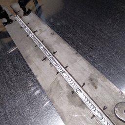 Rafał Małolepszy - Metalowa płyta z precyzyjnym spoiwem spawalniczym, widoczne ślady po mocowaniu. Detal z bliska ukazuje jakość wykonanej spoiny na tle metalowej powierzchni.