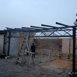 Rafał Małolepszy - Konstrukcja metalowa z drabina w tle, prawdopodobnie w trakcie budowy zadaszenia. Widoczne elementy spawane i surowe ściany budynku.